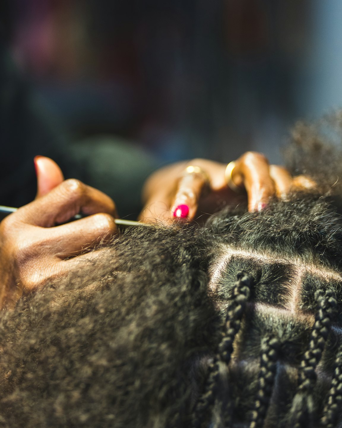Stylist braiding a client's hair with intricate square partings.